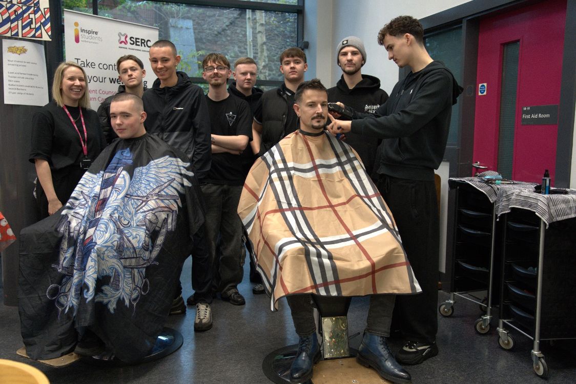 Two clients in barbers' capes with tutor Susan Rooney and the group of barbering students on SERC Lisburn Campus